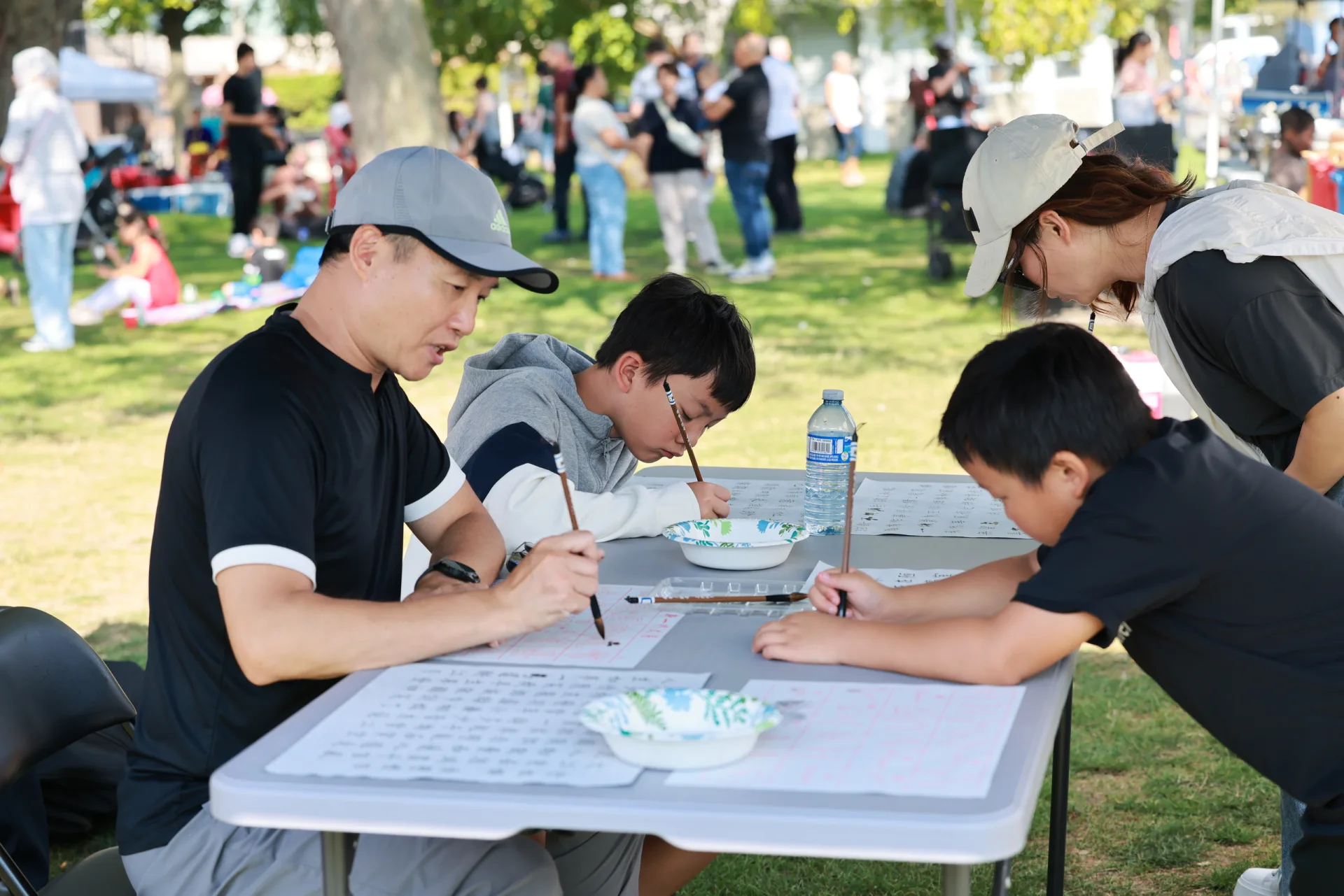 Family and children practicing Chinese calligraphy at an outdoor CCAKD community picnic